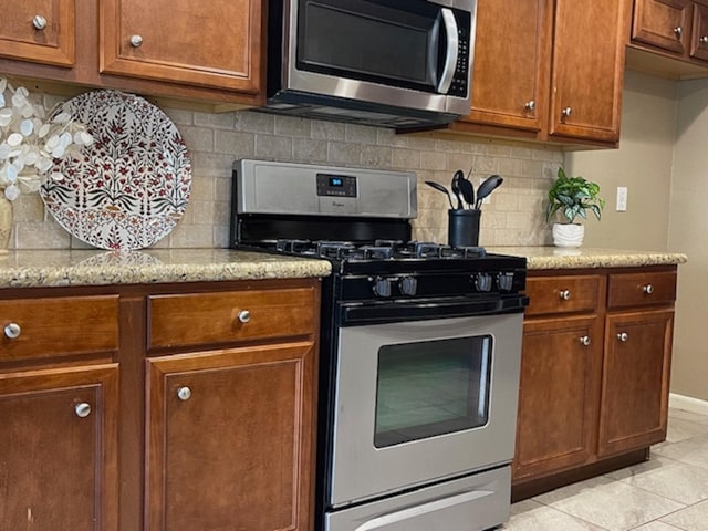 kitchen with appliances with stainless steel finishes, brown cabinetry, backsplash, and light stone countertops