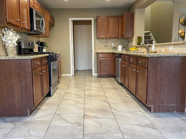 kitchen with appliances with stainless steel finishes, a sink, backsplash, and light stone counters