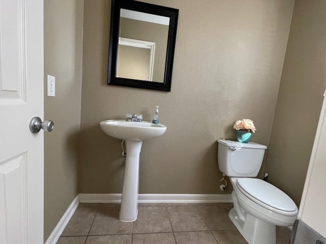 half bath featuring baseboards, toilet, and tile patterned floors