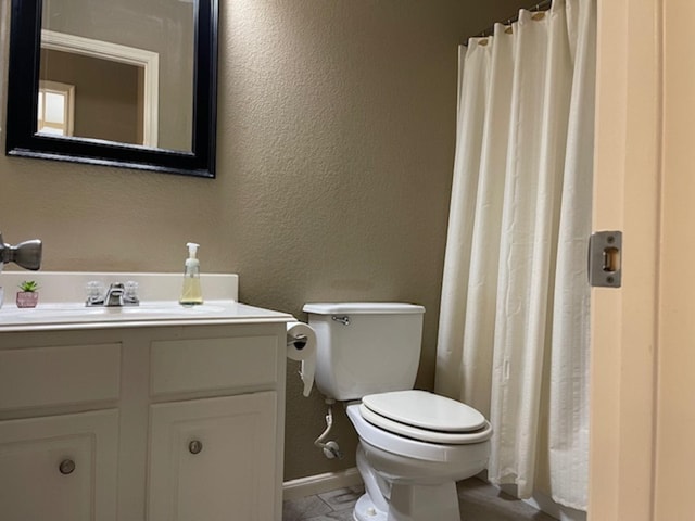 bathroom with a textured wall, toilet, a shower with shower curtain, vanity, and baseboards