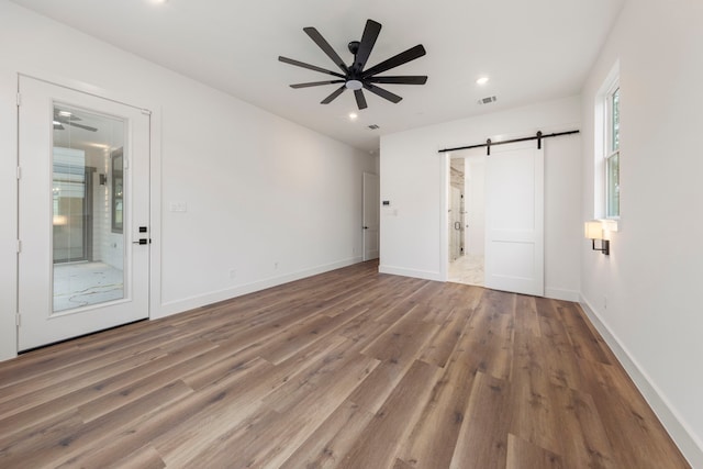 unfurnished bedroom with a barn door, baseboards, visible vents, connected bathroom, and wood finished floors