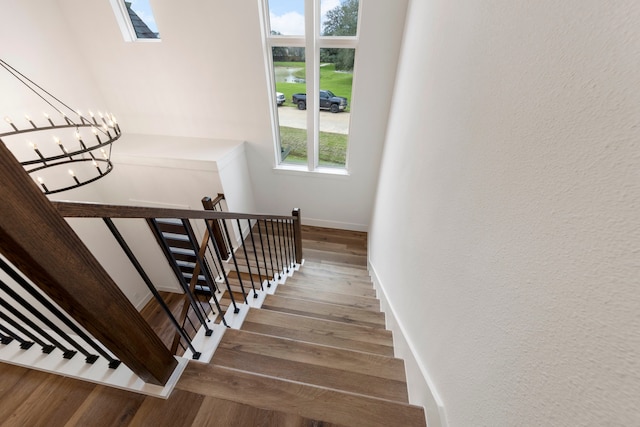 stairs with a notable chandelier, wood finished floors, and baseboards