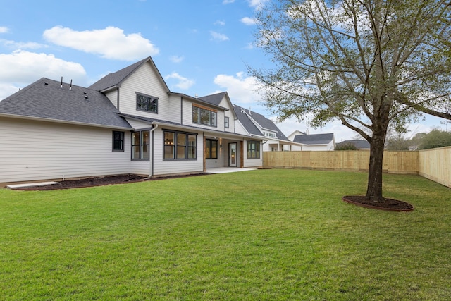 rear view of property with a shingled roof, a patio area, a fenced backyard, and a yard