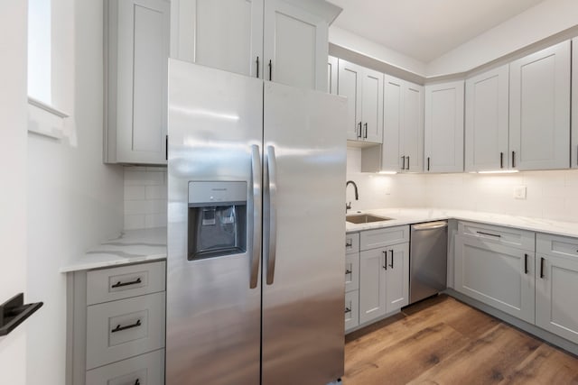 kitchen featuring light stone counters, a sink, appliances with stainless steel finishes, decorative backsplash, and light wood finished floors