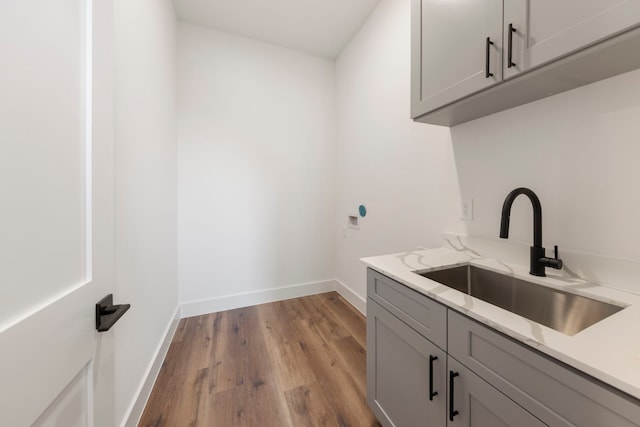 clothes washing area featuring washer hookup, a sink, baseboards, light wood-style floors, and cabinet space