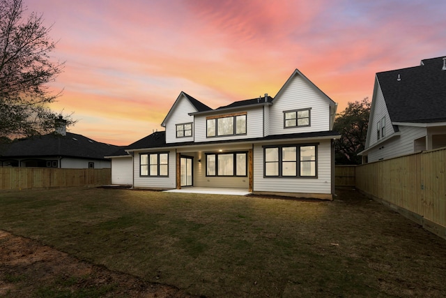 back of property at dusk with a yard, a fenced backyard, and a patio