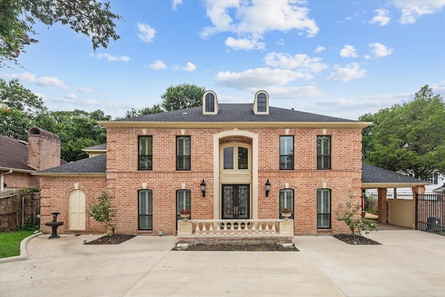 georgian-style home with brick siding, a shingled roof, fence, french doors, and a patio area