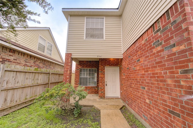 view of exterior entry featuring brick siding, a patio area, and fence