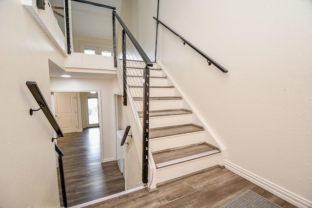 stairway featuring a high ceiling, wood finished floors, and baseboards