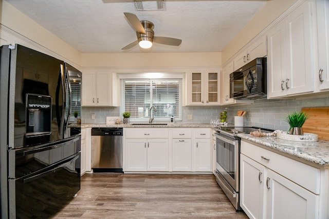 kitchen featuring visible vents, white cabinets, glass insert cabinets, black appliances, and a sink