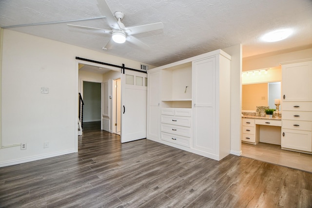 unfurnished bedroom with dark wood-style flooring, a textured ceiling, and a barn door