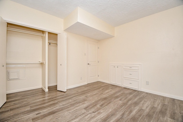 unfurnished bedroom with a closet, a textured ceiling, baseboards, and wood finished floors