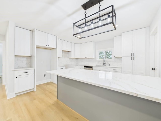 kitchen featuring light stone counters, light wood-style flooring, stainless steel dishwasher, white cabinets, and a sink