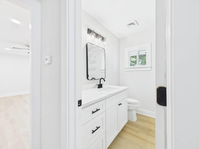 bathroom featuring toilet, wood finished floors, vanity, visible vents, and baseboards