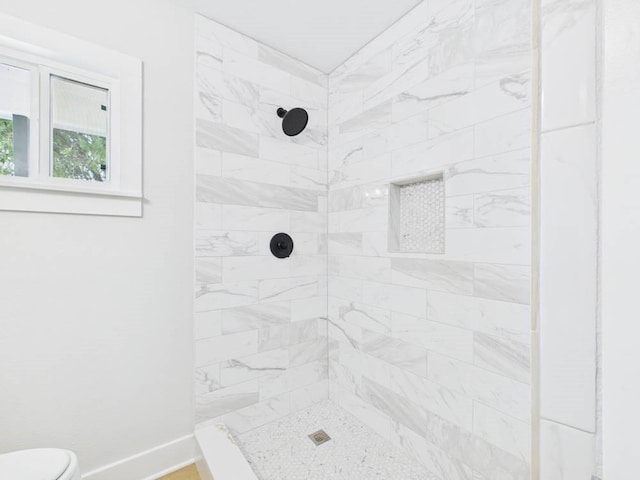 full bath featuring toilet, a tile shower, and baseboards