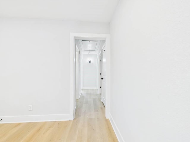 corridor with light wood-type flooring, attic access, and baseboards