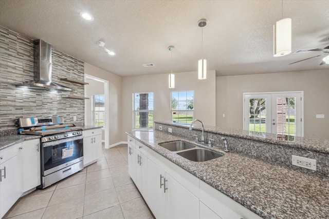 kitchen featuring stainless steel gas range oven, decorative backsplash, wall chimney exhaust hood, a sink, and light tile patterned flooring