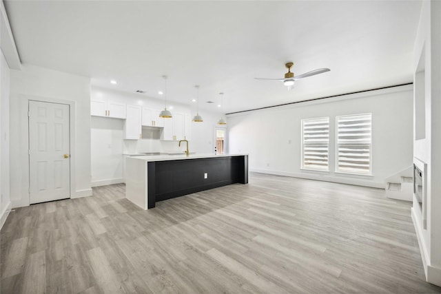 kitchen with light wood-style flooring, a kitchen island with sink, white cabinets, light countertops, and ceiling fan