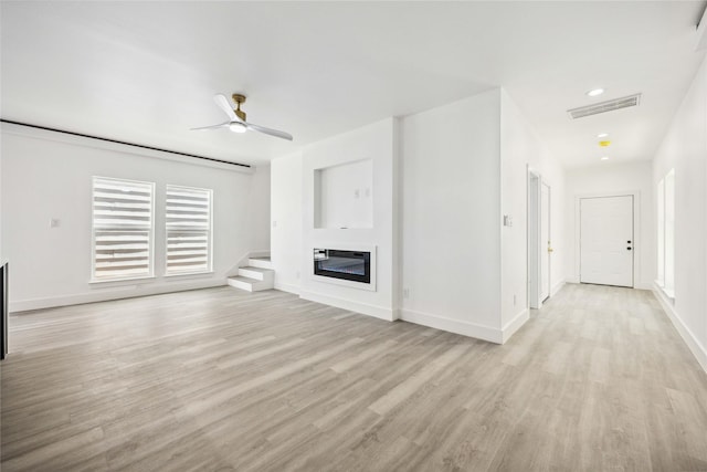 unfurnished living room featuring light wood finished floors, visible vents, ceiling fan, baseboards, and a glass covered fireplace