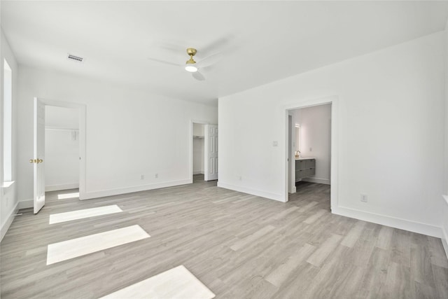 unfurnished bedroom with visible vents, a walk in closet, light wood-style flooring, connected bathroom, and baseboards