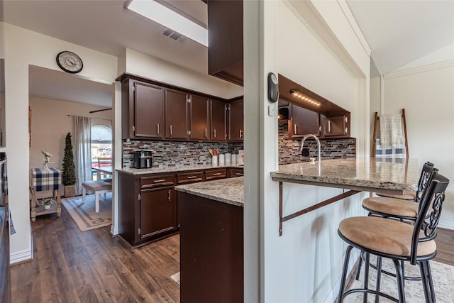 kitchen featuring light stone countertops, dark brown cabinetry, visible vents, and dark wood finished floors