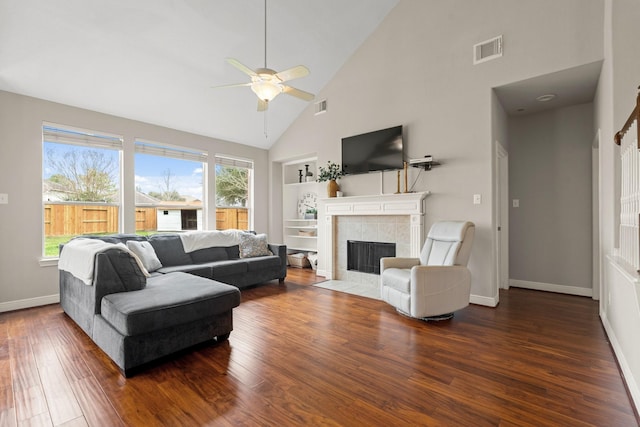 living room with a tile fireplace, visible vents, baseboards, built in features, and dark wood-style floors