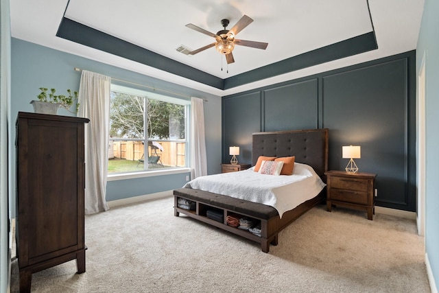 bedroom with light carpet, a raised ceiling, visible vents, and a decorative wall