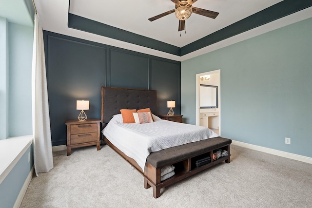 carpeted bedroom with a tray ceiling, ceiling fan, ensuite bath, and baseboards