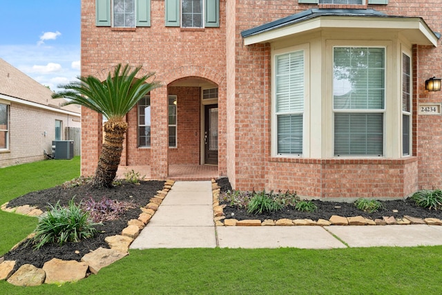 property entrance featuring central air condition unit, a lawn, and brick siding