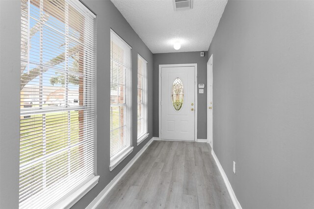 doorway to outside featuring baseboards, visible vents, a healthy amount of sunlight, a textured ceiling, and light wood-type flooring