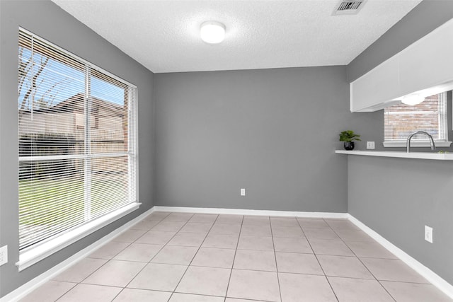 unfurnished dining area with a textured ceiling, light tile patterned floors, a sink, visible vents, and baseboards