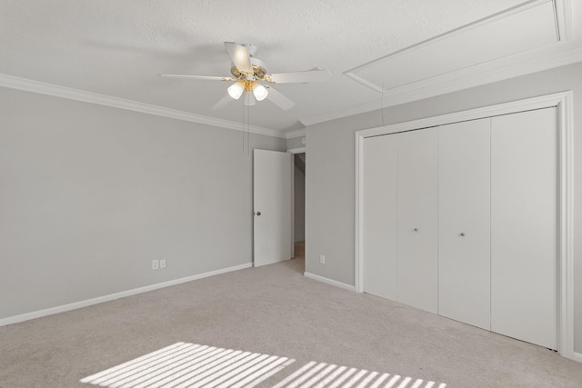 unfurnished bedroom featuring light carpet, attic access, baseboards, ornamental molding, and a closet