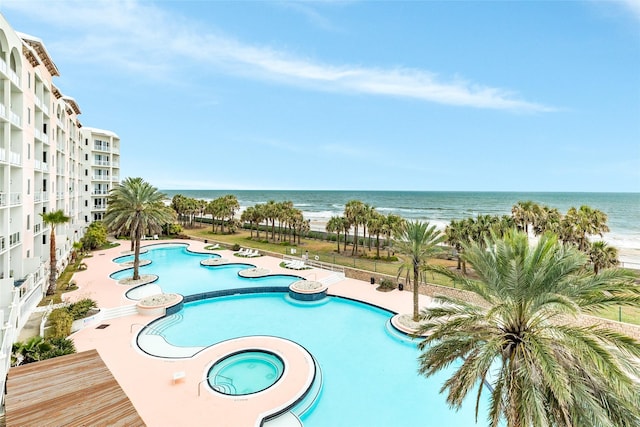 pool with a view of the beach, a community hot tub, a water view, and a patio