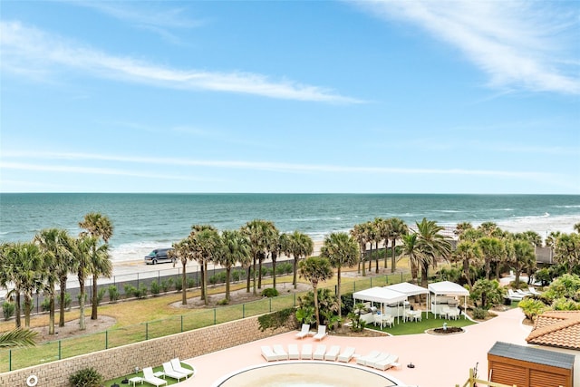 property view of water with fence, a fire pit, and a beach view