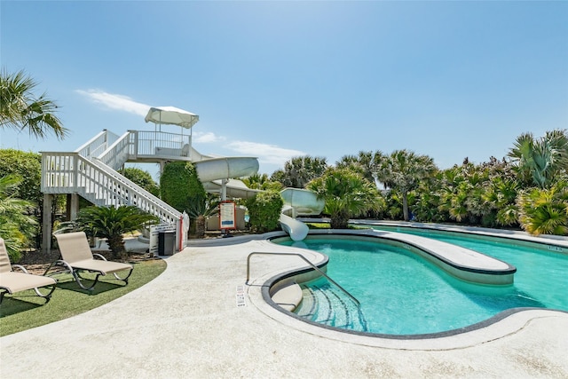 community pool with a water slide, a patio, and stairs