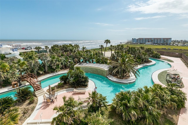 community pool with a water view, a patio area, and fence
