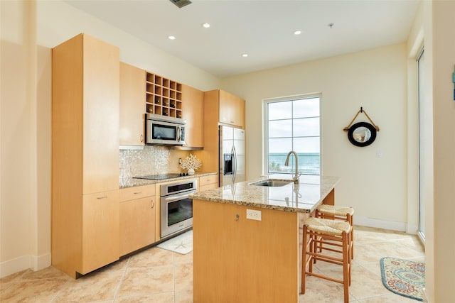 kitchen featuring a center island with sink, a breakfast bar area, light stone countertops, stainless steel appliances, and a sink