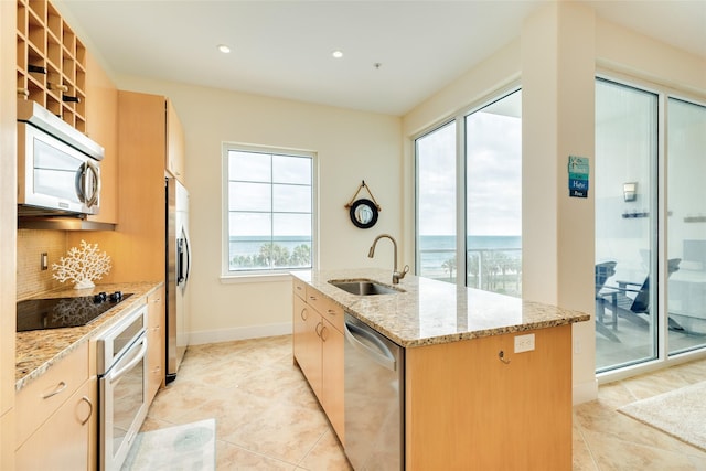 kitchen featuring decorative backsplash, an island with sink, appliances with stainless steel finishes, light stone counters, and a sink