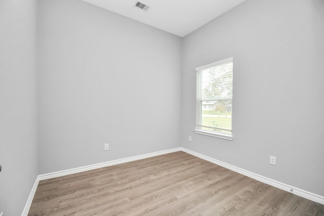 spare room with light wood-type flooring, visible vents, and baseboards