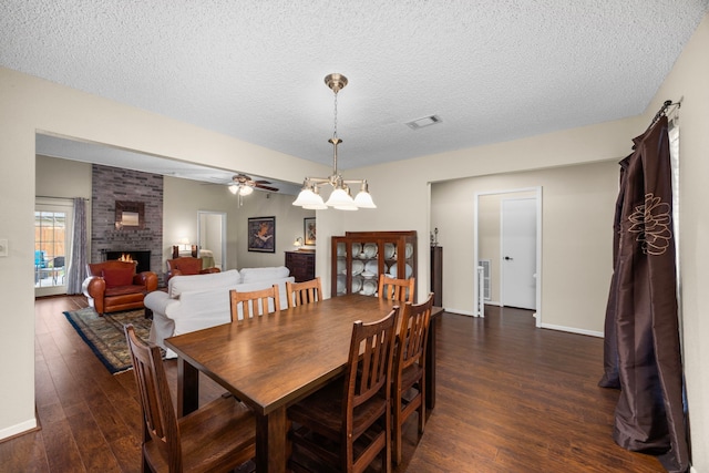 dining area featuring dark wood finished floors, visible vents, a brick fireplace, a textured ceiling, and baseboards