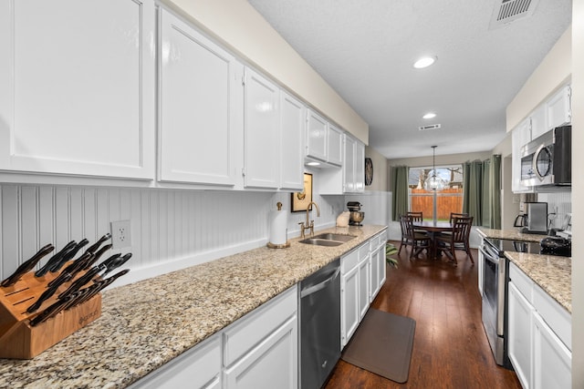 kitchen with decorative light fixtures, stainless steel appliances, visible vents, white cabinetry, and a sink