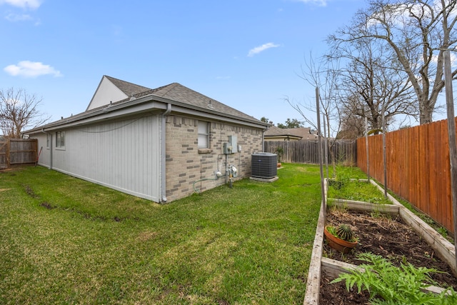 view of side of home with a yard, brick siding, a fenced backyard, and a vegetable garden