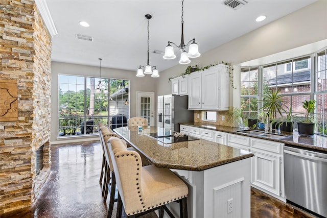 kitchen with decorative light fixtures, appliances with stainless steel finishes, a sink, a kitchen island, and dark stone countertops