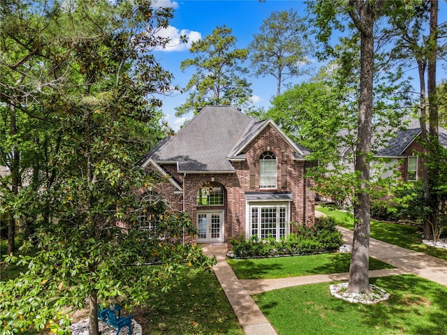 traditional-style home featuring brick siding, a shingled roof, a front lawn, and french doors