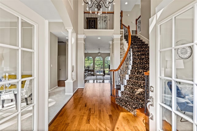 entrance foyer featuring baseboards, wood finished floors, stairs, ornate columns, and a chandelier