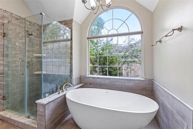 full bath featuring lofted ceiling, tile walls, a freestanding bath, a stall shower, and an inviting chandelier