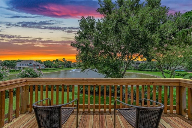 deck at dusk with a water view and a lawn