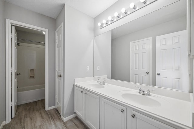 bathroom featuring double vanity, shower / bathing tub combination, a sink, and wood finished floors