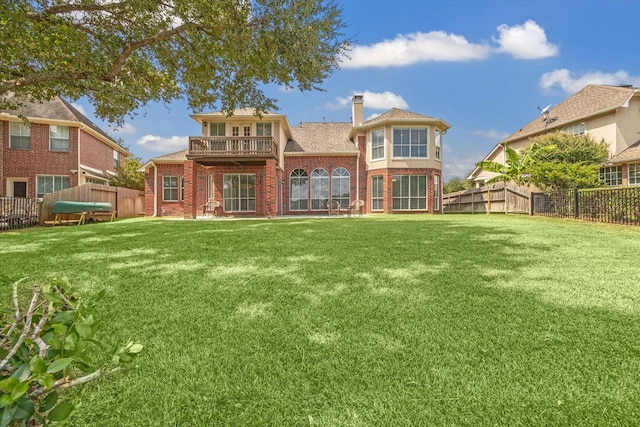 back of house with a lawn, a balcony, a fenced backyard, a chimney, and brick siding