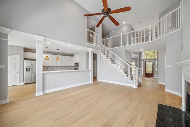 unfurnished living room featuring decorative columns, stairway, a fireplace with flush hearth, light wood-type flooring, and baseboards